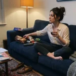 Femme assise sur canapé bleu, tenant une boisson, avec snacks.